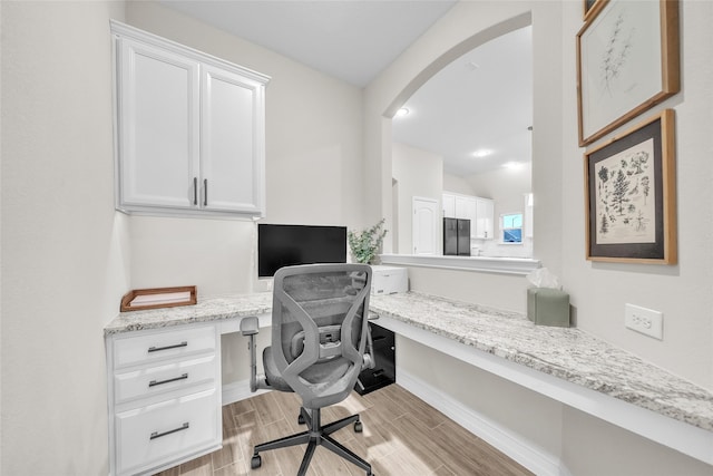 home office with built in desk, wood finish floors, arched walkways, and baseboards