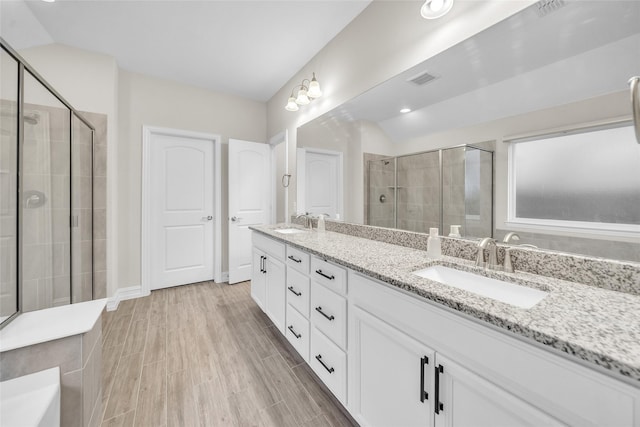 bathroom with double vanity, wood finished floors, a stall shower, and a sink