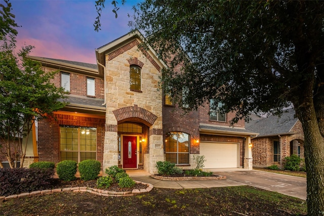 view of front of property with a garage, brick siding, driveway, and stone siding