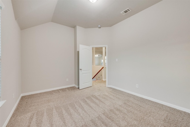 empty room with lofted ceiling, visible vents, light colored carpet, and baseboards