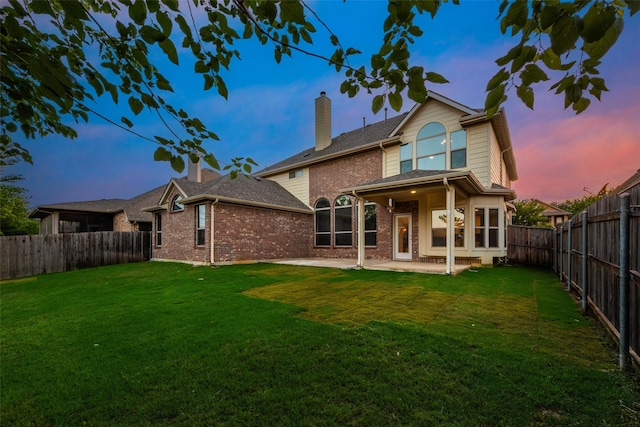 back of property at dusk with a chimney, brick siding, a fenced backyard, and a yard