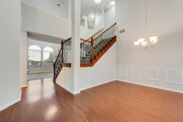 stairway with wood finished floors, an inviting chandelier, baseboards, visible vents, and a high ceiling