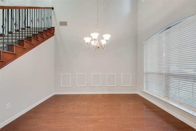 unfurnished dining area featuring visible vents, baseboards, a towering ceiling, wood finished floors, and a notable chandelier