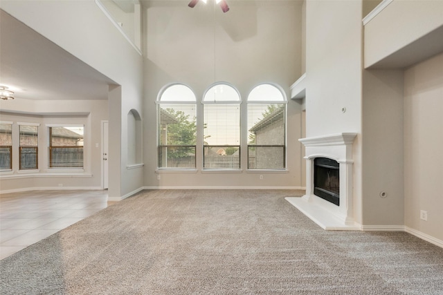 unfurnished living room with ceiling fan, carpet, a towering ceiling, and a fireplace with raised hearth