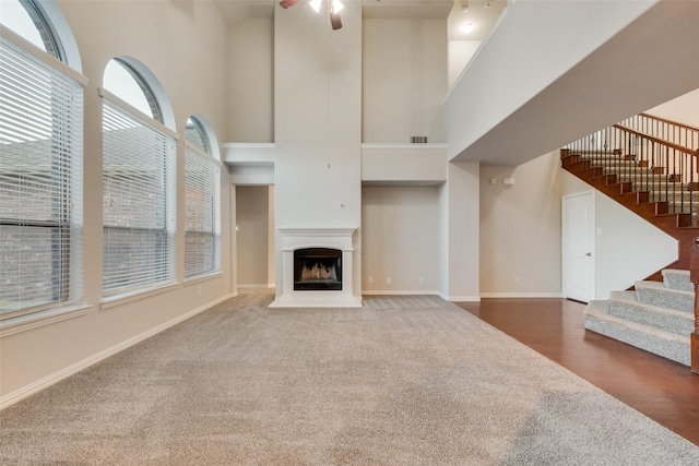 unfurnished living room with a healthy amount of sunlight, ceiling fan, stairs, and a towering ceiling