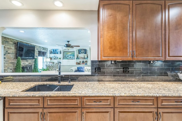 kitchen featuring light stone counters, a sink, decorative backsplash, and a ceiling fan