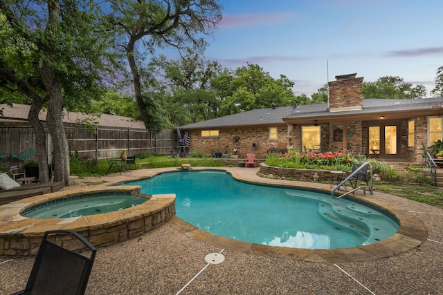 pool at dusk featuring fence, a pool with connected hot tub, and a patio area