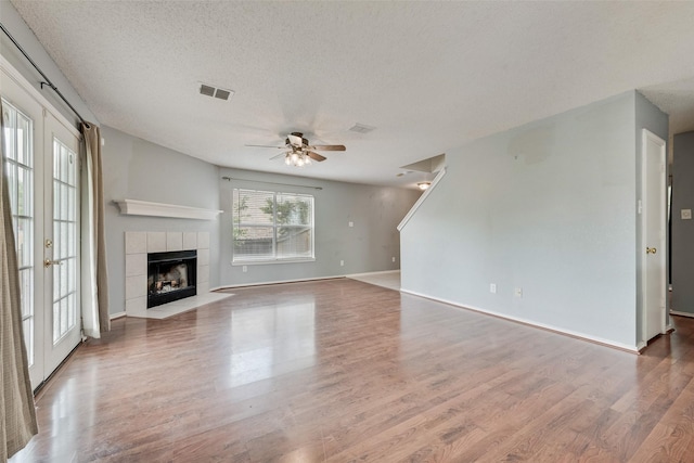 unfurnished living room with ceiling fan, a textured ceiling, visible vents, a fireplace, and wood finished floors