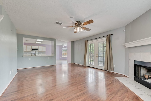 unfurnished living room with visible vents, ceiling fan, wood finished floors, and a tiled fireplace