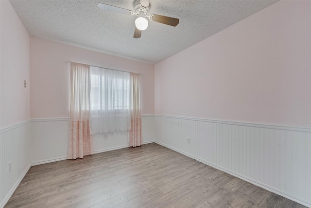 unfurnished room featuring a textured ceiling, ceiling fan, wood finished floors, and a wainscoted wall