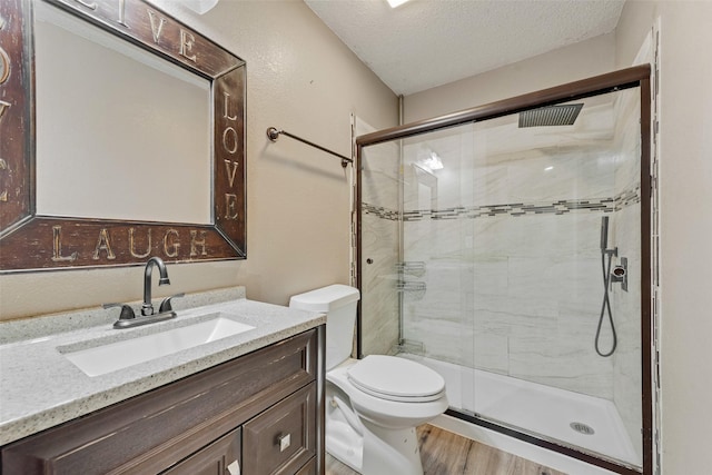 bathroom with vanity, wood finished floors, toilet, a textured ceiling, and a stall shower