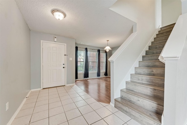 foyer with baseboards, a textured ceiling, light tile patterned floors, and stairway