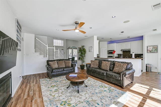 12165 Shoal Creek Dr, Frisco, TX 75035 - living room featuring arched walkways, stairs, ceiling fan, light wood-style flooring, and baseboards