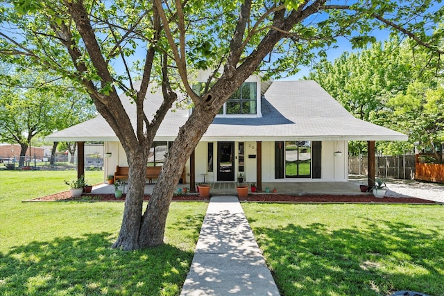 view of front facade with a front lawn, a shingled roof, covered porch, and fence