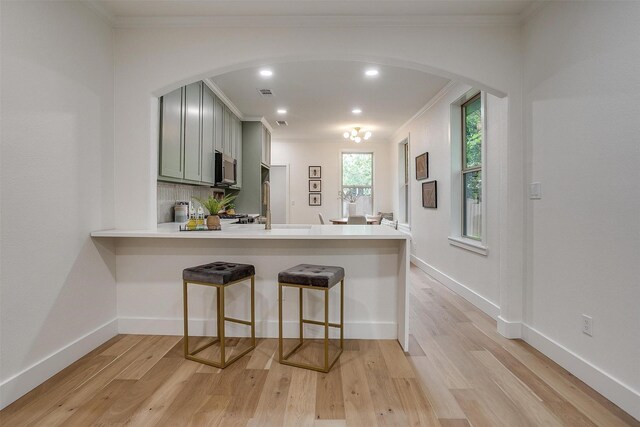 5105 Birchman Ave, Fort Worth, TX 76107 - kitchen with stainless steel microwave, a breakfast bar area, light wood-style flooring, light countertops, and arched walkways