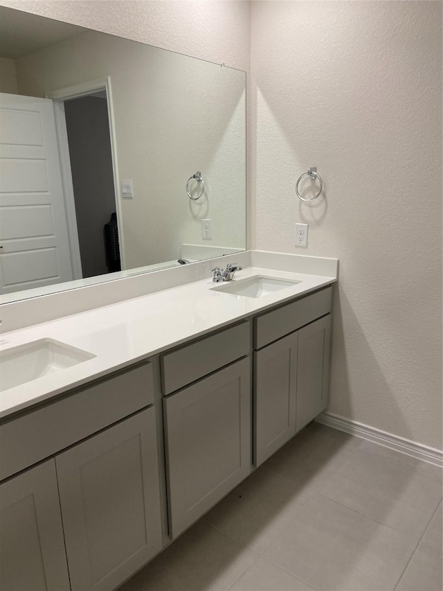 bathroom featuring tile patterned flooring, a sink, double vanity, and baseboards