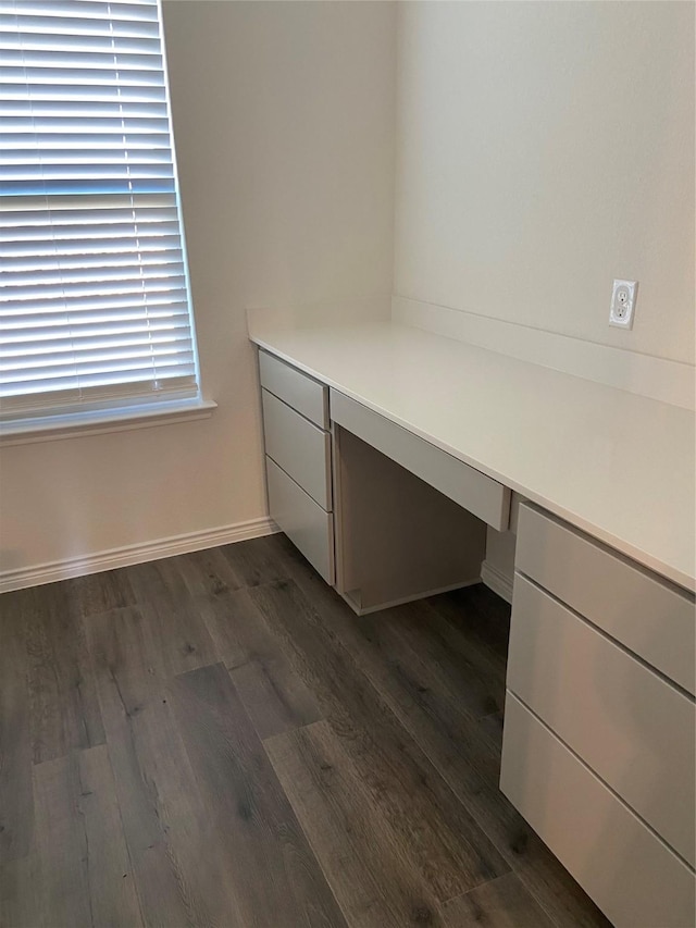 unfurnished office with dark wood-type flooring, built in desk, and baseboards