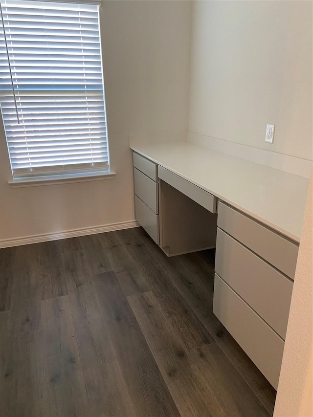 unfurnished office featuring built in desk, dark wood-style floors, and baseboards