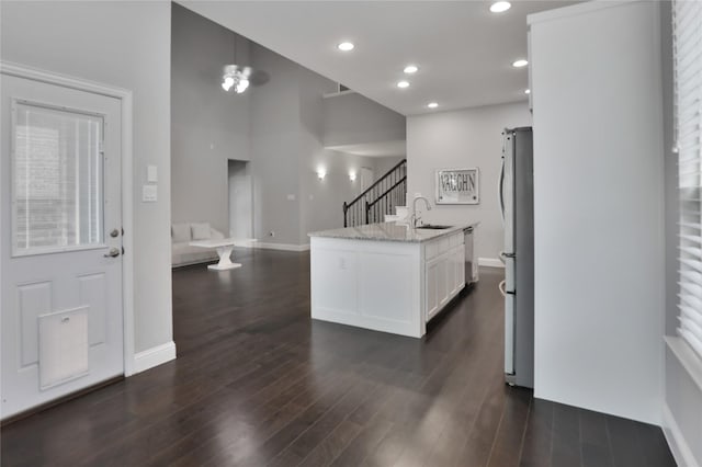 kitchen with light stone counters, stainless steel appliances, white cabinets, a sink, and dark wood-type flooring