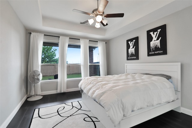 bedroom with a ceiling fan, wood finished floors, a raised ceiling, and baseboards