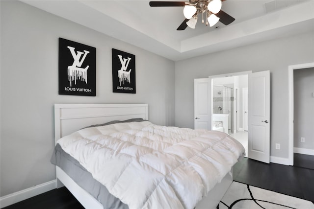bedroom with dark wood-type flooring, a tray ceiling, connected bathroom, and baseboards