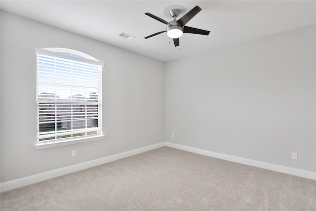 carpeted spare room with visible vents, a healthy amount of sunlight, a ceiling fan, and baseboards