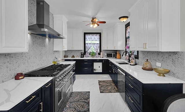 kitchen featuring stainless steel appliances, a sink, dark cabinetry, and wall chimney range hood