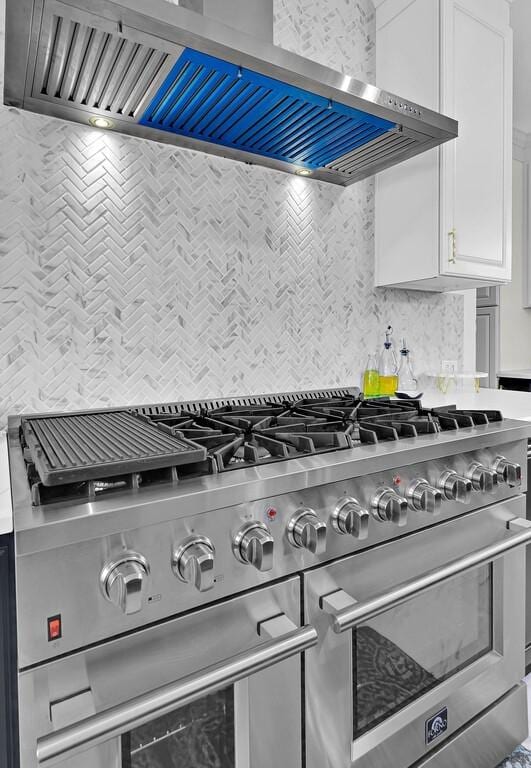 details featuring stovetop, white cabinetry, backsplash, and wall chimney exhaust hood