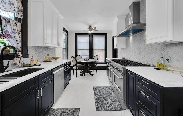 kitchen with white cabinetry, a sink, dark cabinets, stainless steel appliances, and wall chimney exhaust hood