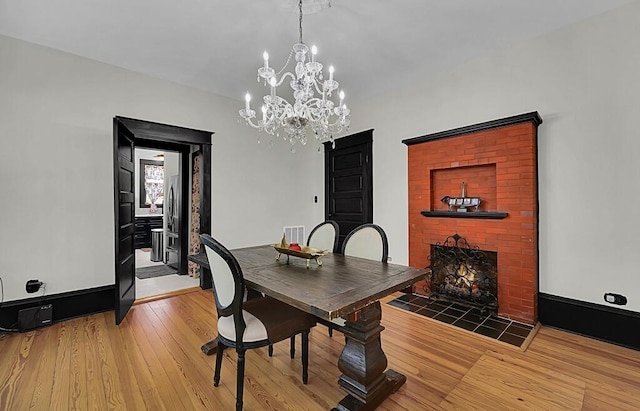 dining room featuring an inviting chandelier, light wood-style floors, visible vents, and a brick fireplace