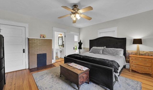 bedroom featuring ceiling fan, connected bathroom, light wood finished floors, and a brick fireplace