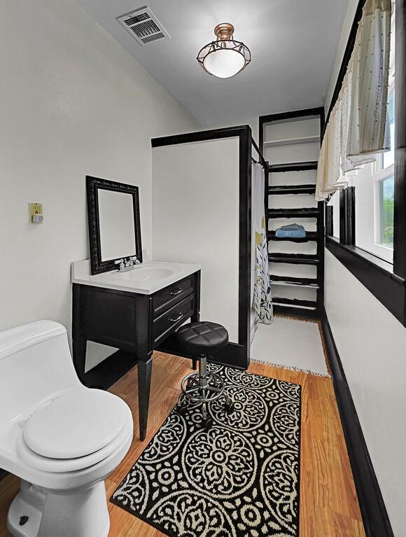 bathroom with vanity, toilet, visible vents, a shower, and wood finished floors