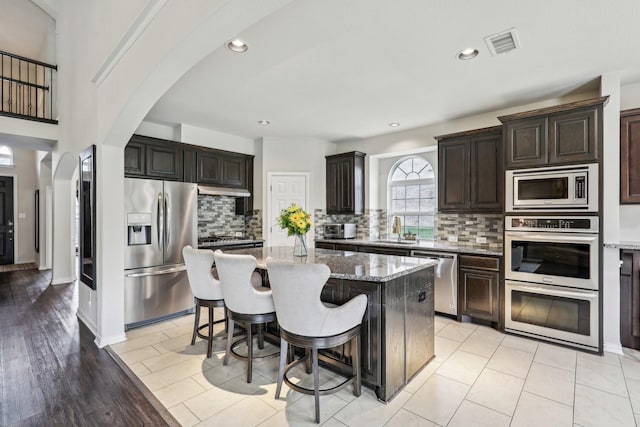 kitchen with arched walkways, light stone counters, appliances with stainless steel finishes, a sink, and visible vents