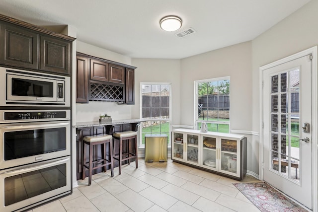 kitchen featuring a breakfast bar area, stainless steel appliances, light tile patterned floors, dark brown cabinets, and visible vents