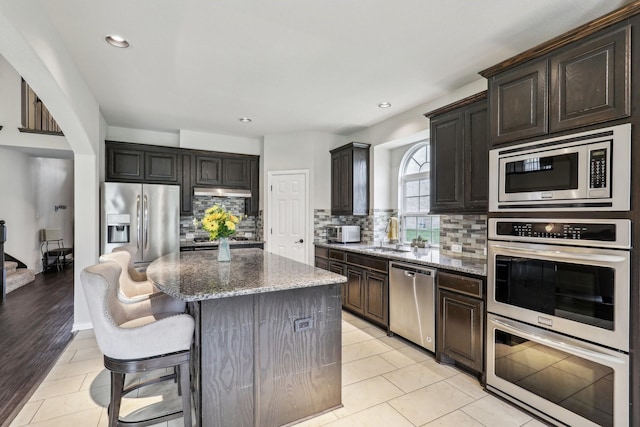 kitchen featuring a sink, stainless steel appliances, backsplash, a kitchen island, and stone countertops