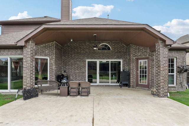 rear view of house featuring a patio, a chimney, a shingled roof, and brick siding
