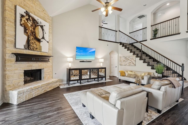 living area featuring stairway, ceiling fan, dark wood-type flooring, high vaulted ceiling, and a stone fireplace