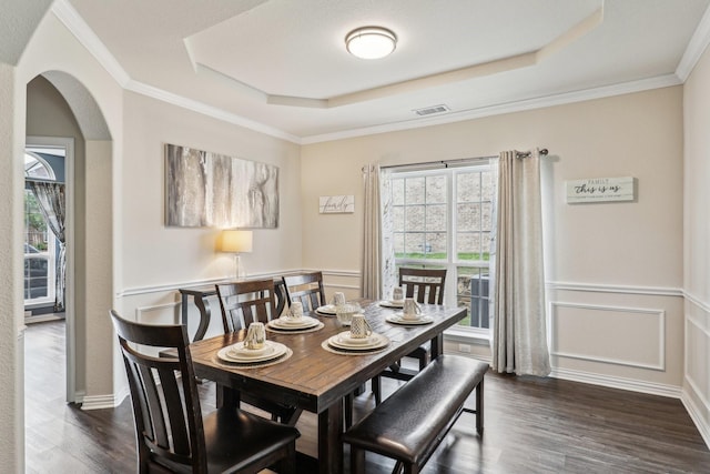 dining room with visible vents, a tray ceiling, dark wood-style floors, arched walkways, and wainscoting