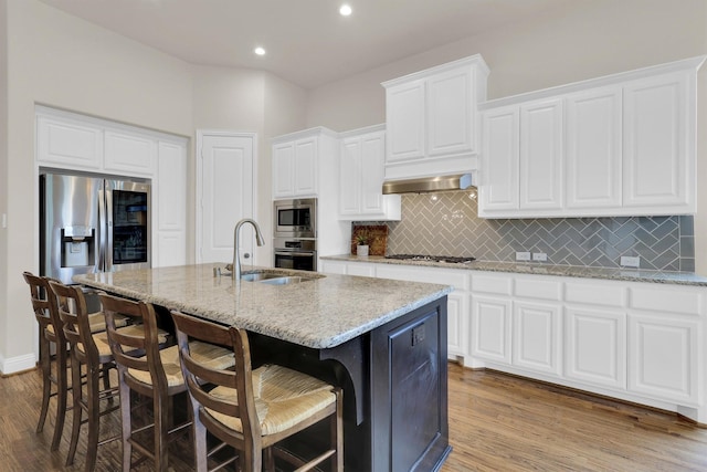 3555 Fieldview Ct, Celina, TX 75009 - kitchen featuring stainless steel appliances, wood finished floors, a center island with sink, backsplash, and light stone countertops