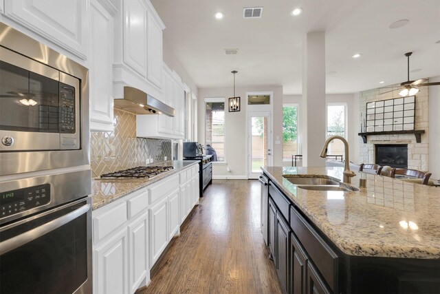 kitchen featuring appliances with stainless steel finishes, a sink, an island with sink, decorative backsplash, and wood finished floors