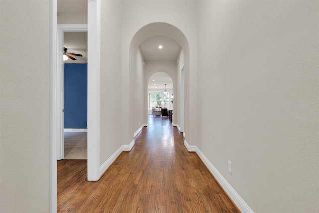 hall with baseboards, arched walkways, and wood finished floors
