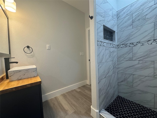 bathroom with vanity, tiled shower, wood finished floors, and baseboards