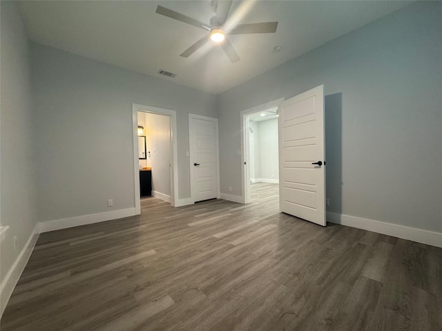 unfurnished bedroom with dark wood-style floors, ensuite bathroom, visible vents, and baseboards