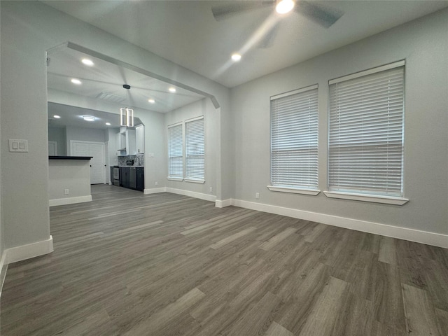 unfurnished living room featuring ceiling fan, dark wood-style flooring, and baseboards