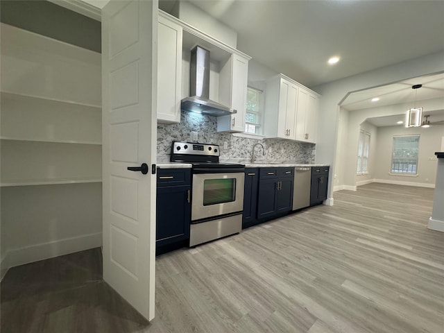 kitchen with wall chimney range hood, a sink, light wood-style floors, stainless steel appliances, and baseboards