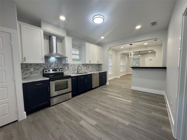 kitchen featuring tasteful backsplash, appliances with stainless steel finishes, wall chimney range hood, white cabinetry, and visible vents