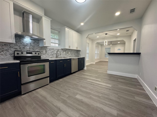 kitchen with tasteful backsplash, a sink, stainless steel appliances, light wood finished floors, and wall chimney exhaust hood