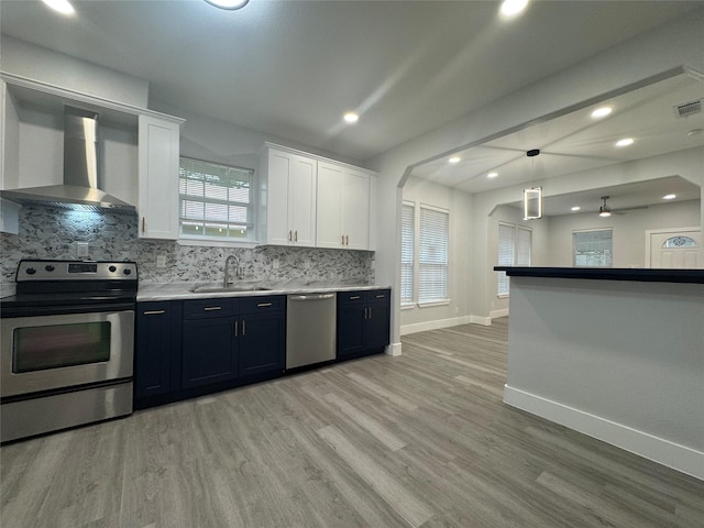 kitchen with arched walkways, decorative backsplash, stainless steel appliances, a sink, and wall chimney exhaust hood