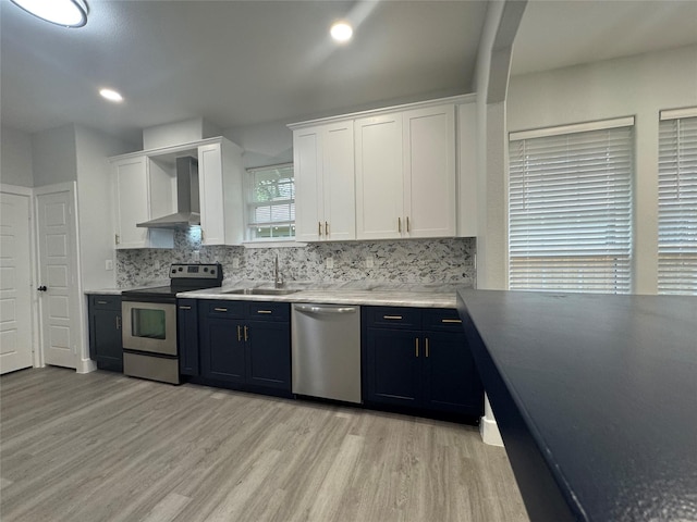 kitchen featuring white cabinetry, stainless steel appliances, wall chimney exhaust hood, and light wood-style flooring