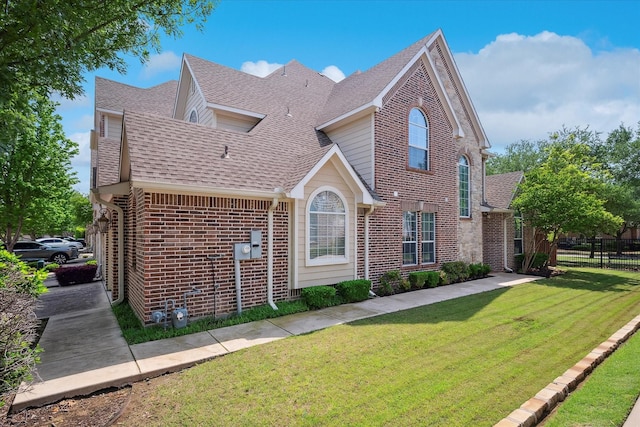 view of front of property featuring brick siding, fence, a shingled roof, and a front lawn